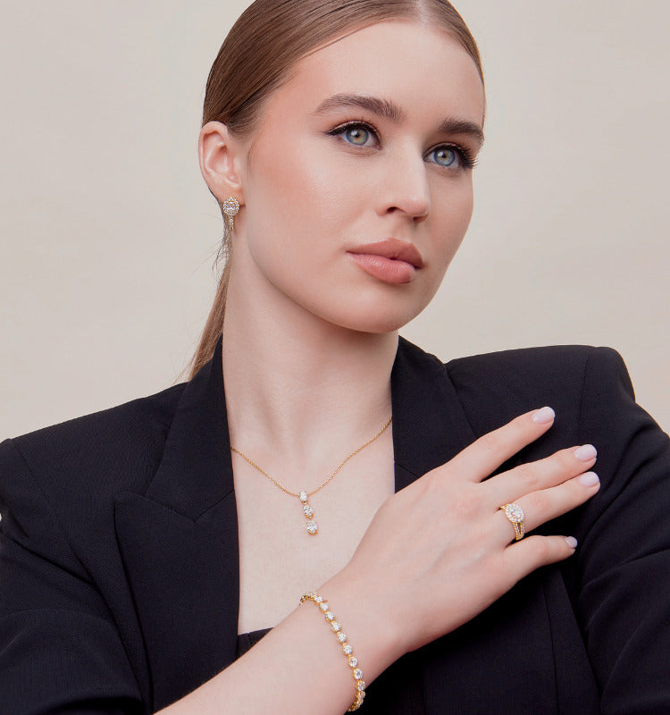 Woman wearing gold jewelry including a necklace, ring, and bracelet against a neutral background