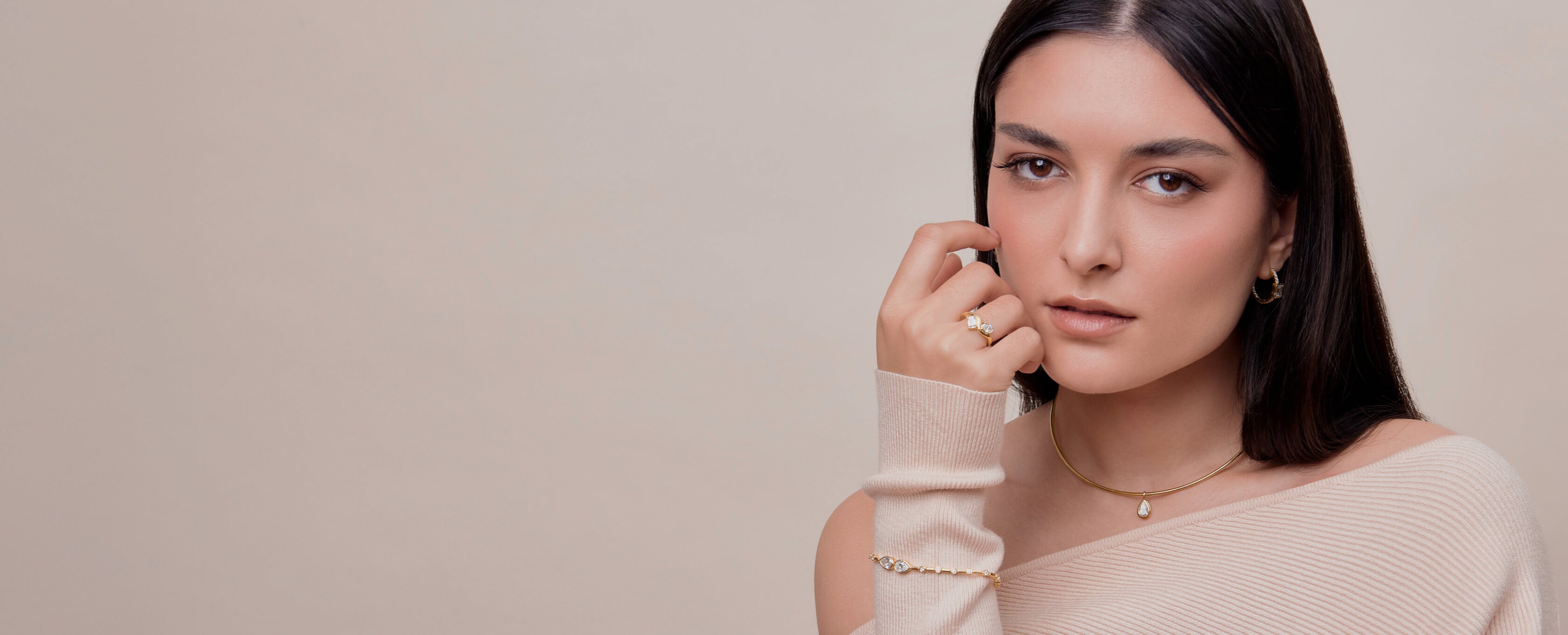 Woman wearing gold jewelry including a necklace, ring, and bracelet against a neutral background